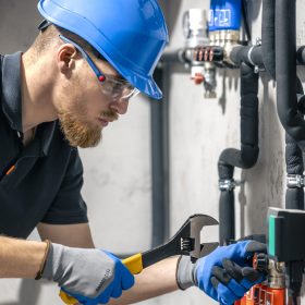 A man installs a heating system in a house and checks the pipes with a wrench. Adjusting heating valves in a residential building. A plumbing and heating technician works.